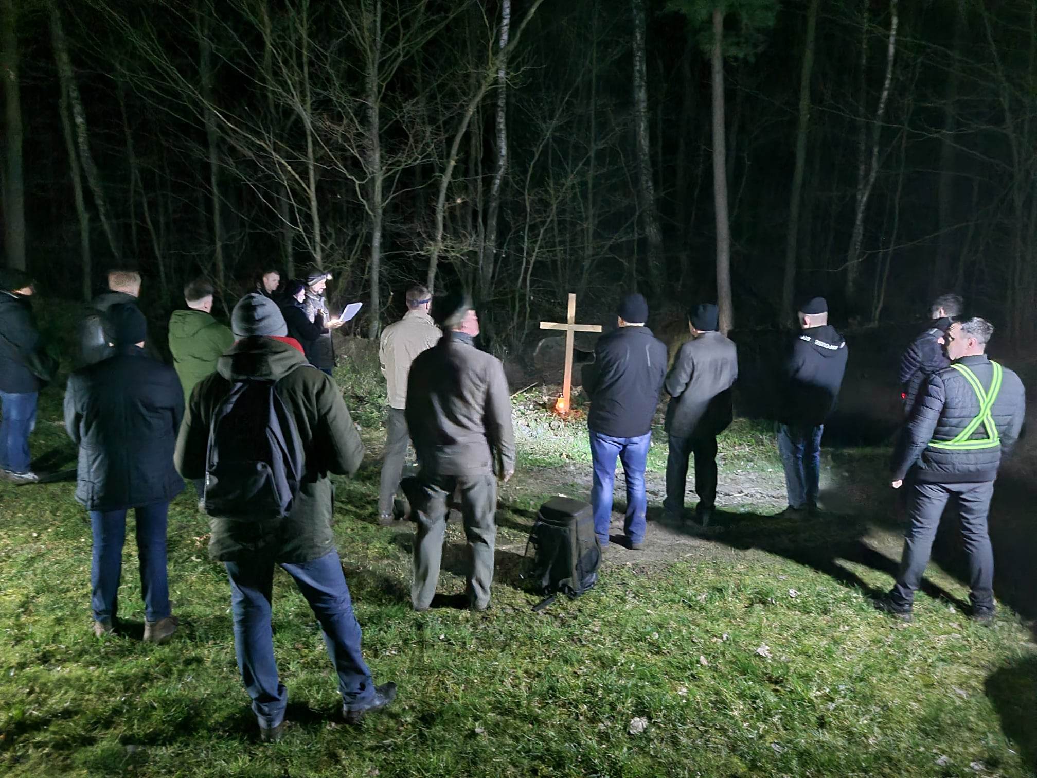 Uczestnicy Męskiej Drogi Krzyżowej zgromadzeni nocą przy drewnianym krzyżu w lesie.