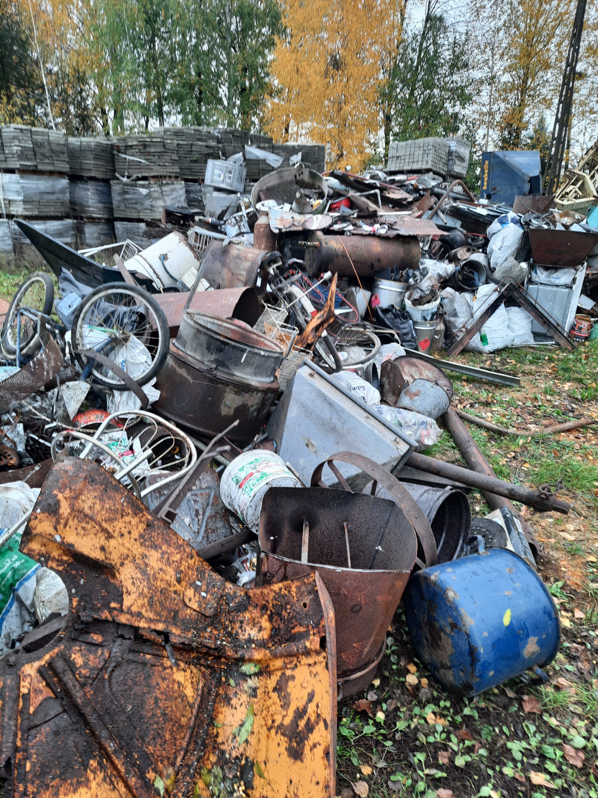 Zbierka złomu w gminie Brańsk. Na zdjęciu przedstawiono stos metalowych przedmiotów, w tym beczek i części maszyn, gromadzący się na terenie gminy.