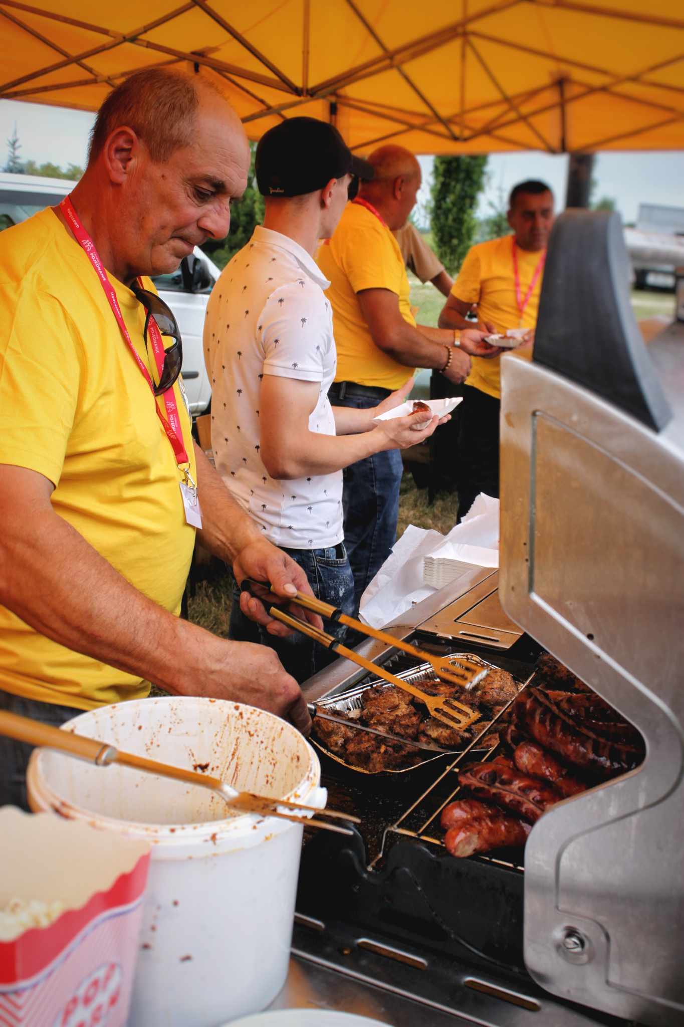 Mężczyzna obsługuje grill z mięsem na wydarzeniu. Osobista interakcja podczas imprezy rodzinnej.