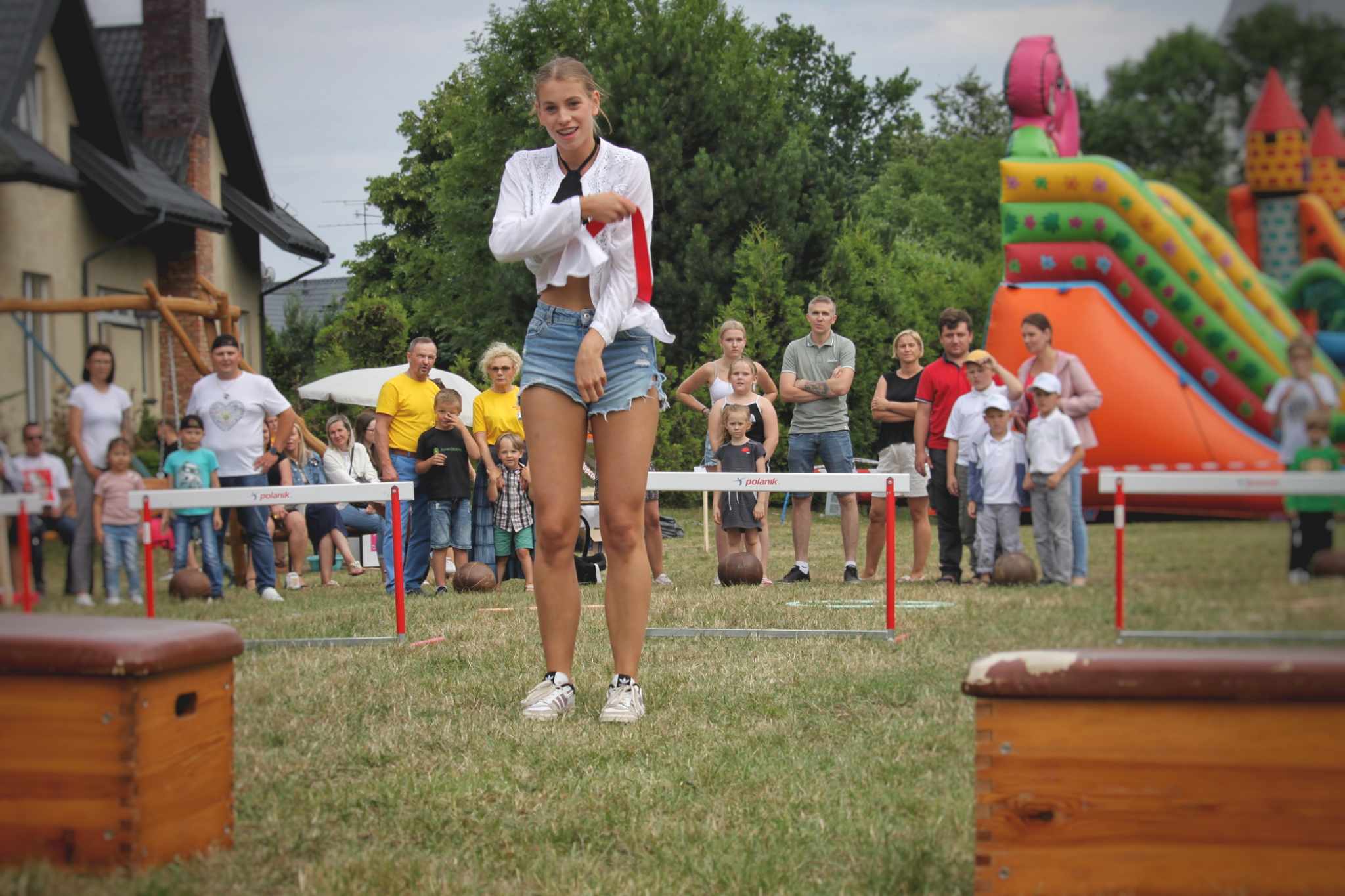 Kobieta stoi przed przeszkodami podczas wydarzenia plenerowego. W tle widoczna publiczność i atrakcje.