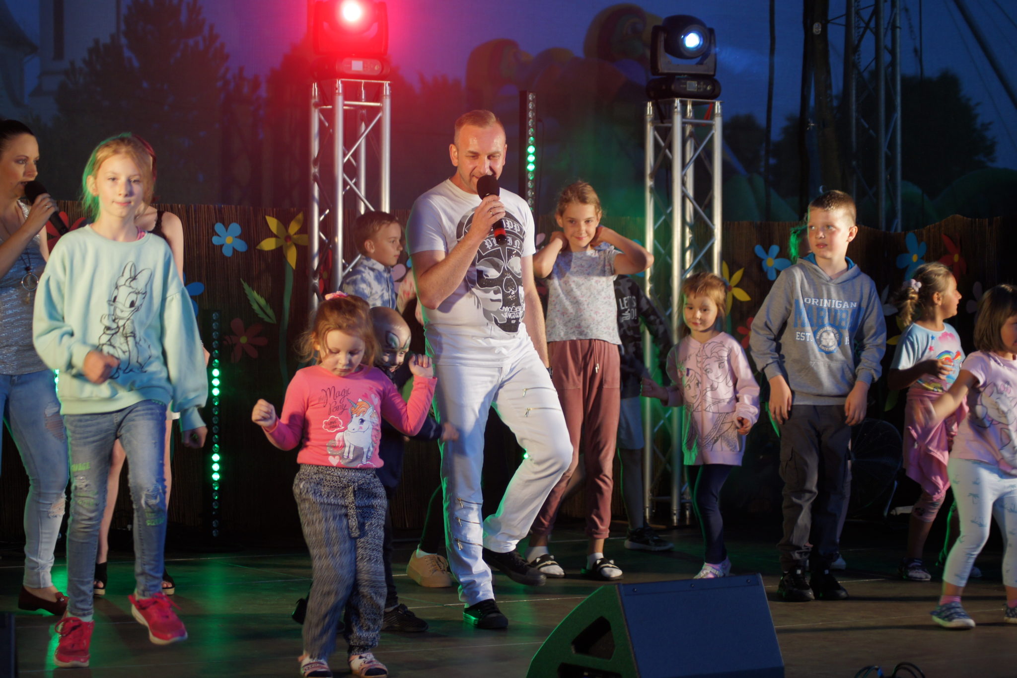 Zdjęcie z wydarzenia IV Dzień Rodziny, 24 lipca 2022 r., na którym grupa dzieci i dorosłych śpiewa i tańczy na scenie.