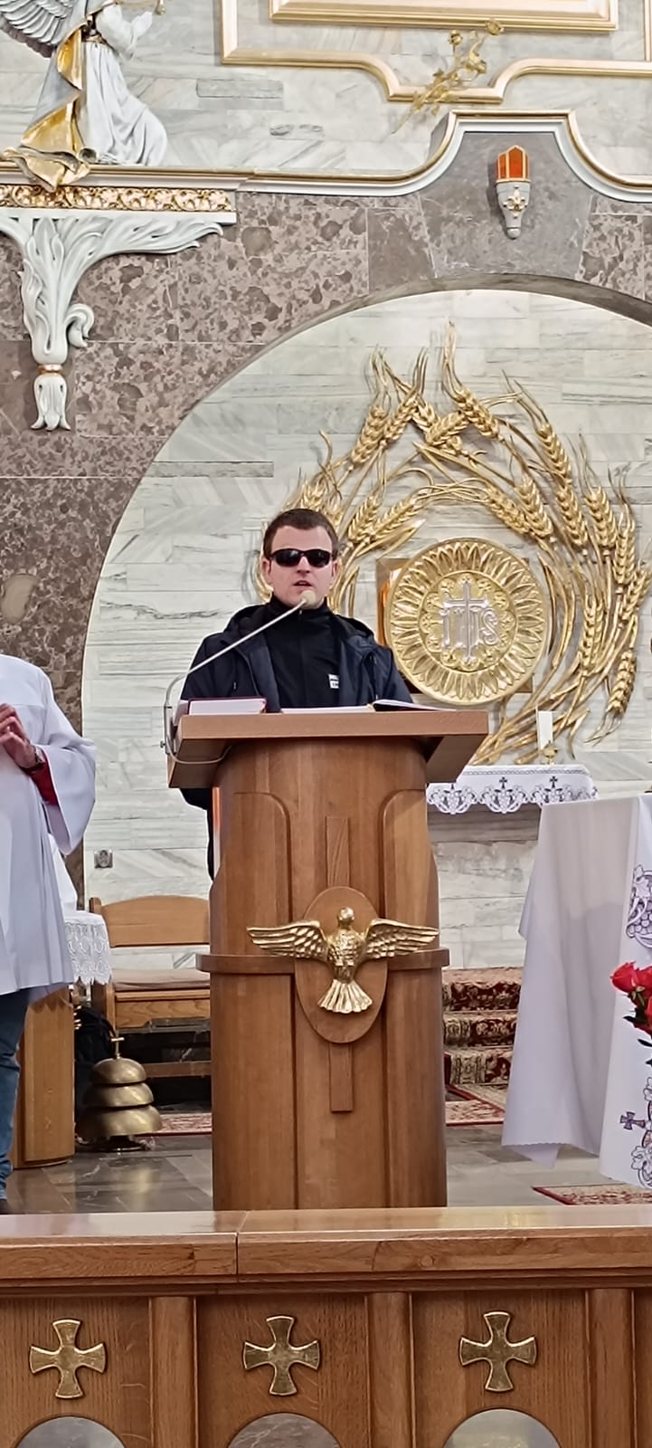 Obraz przedstawia mężczyznę w kościele podczas Msz świętej. W tle znajduje się ołtarz z obrazem Chrystusa Pańskiego.