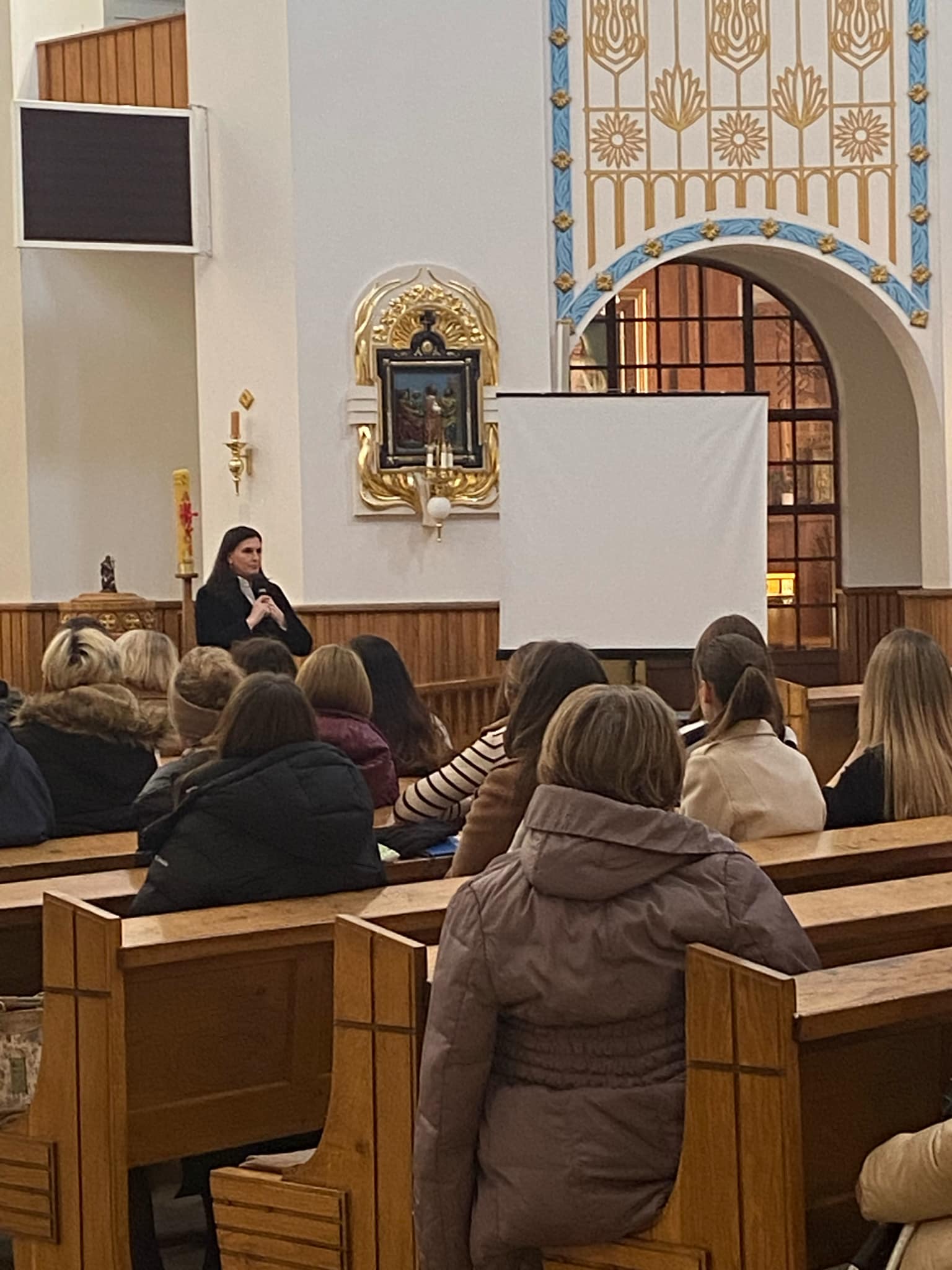 Grupa osób słucha wystąpienia w kościele.