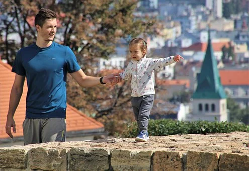 Mężczyzna i dziecko spacerują po murze, z widokiem na miasto. Oznacza to wsparcie i interakcję między rodzicami a dziećmi.